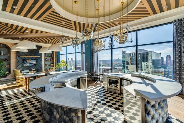 Luxury high-rise kitchen with striped ceiling, curved islands, geometric pendant lights, and panoramic city skyline views through floor-to-ceiling windows.