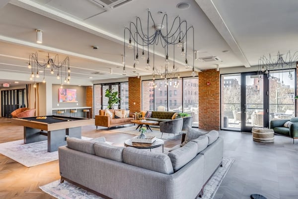 Modern open-plan living room with gray sectional sofa, dining table, wall-mounted TV, and balcony overlooking city skyline.